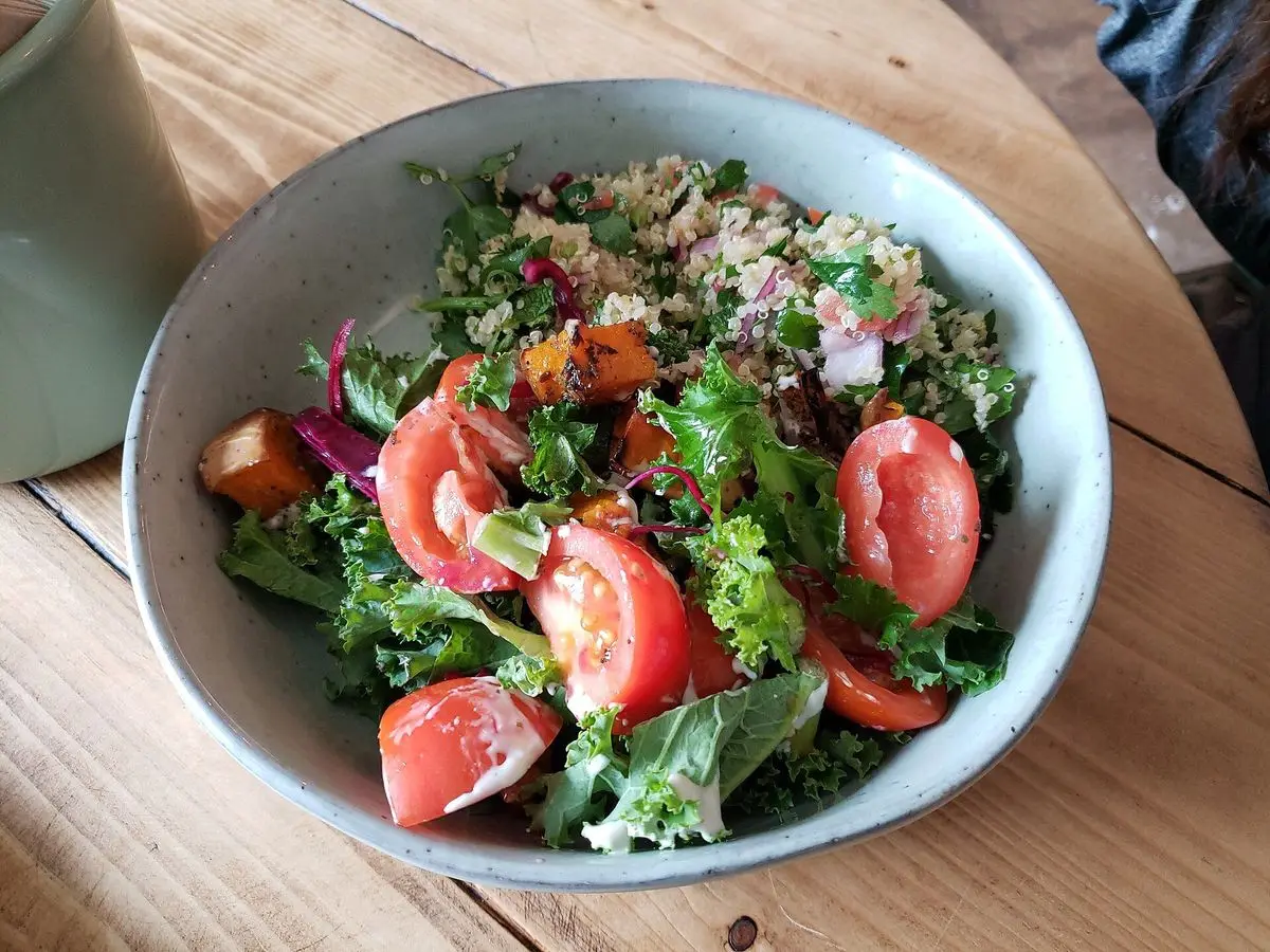 Cuenco de ensalada de hojas verdes con tomate, calabaza asada y semillas