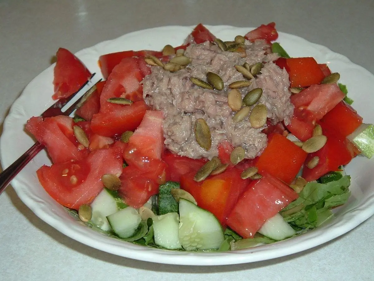 Plato blanco con ensalada de tomate en gajos, atún, pepino y semillas