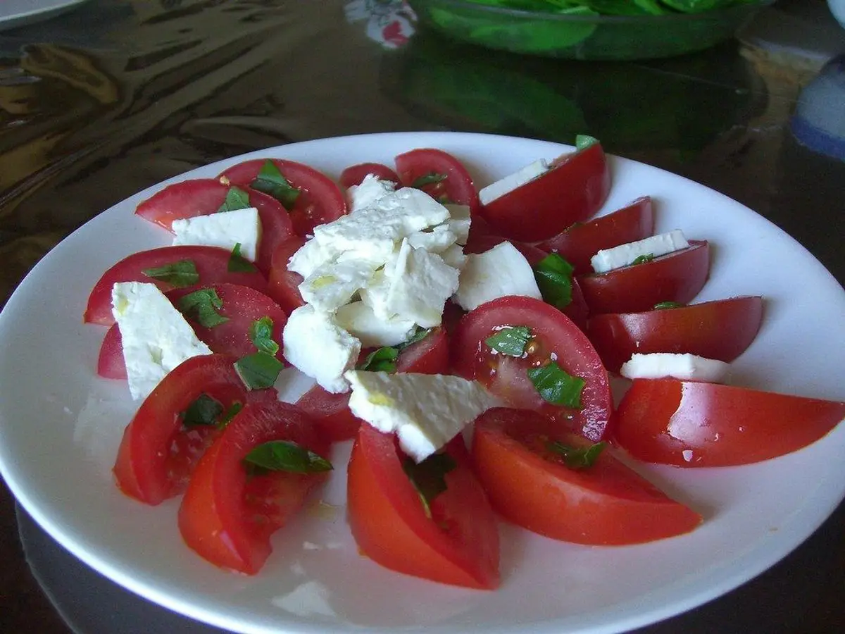 Plato blanco con rodajas de tomate, queso fresco desmenuzado y hojas de albahaca