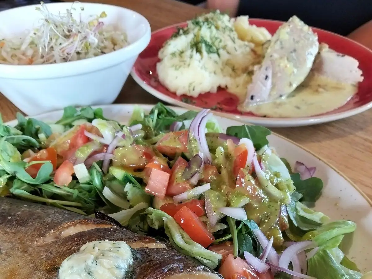 Trucha a la plancha con mantequilla de hierbas sobre ensalada de tomate, cebolla y hojas verdes