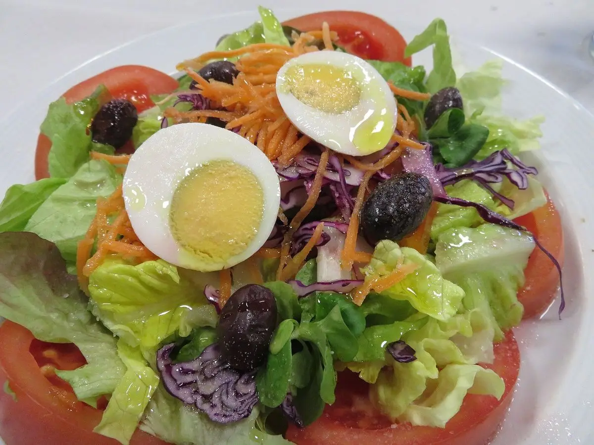 Ensalada con medio huevo cocido, lechuga, zanahoria rallada, lombarda, aceitunas y tomate