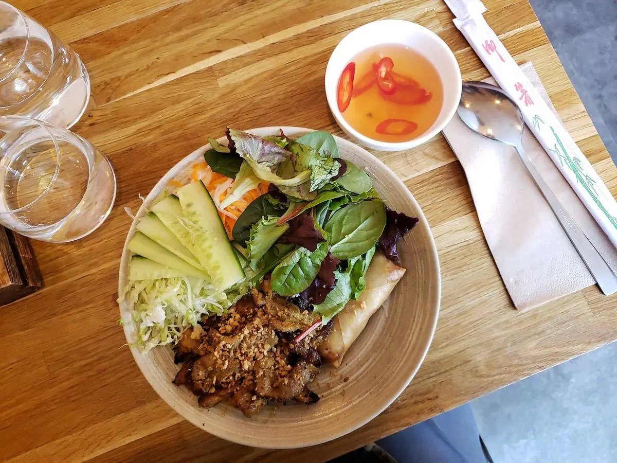 Cuenco vietnamita de fideos de arroz con hierbas frescas, carne y salsa picante sobre una mesa de madera