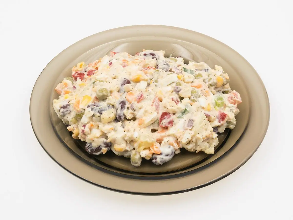 Ensaladilla con patata, zanahoria y mayonesa servida en un plato oscuro sobre fondo blanco