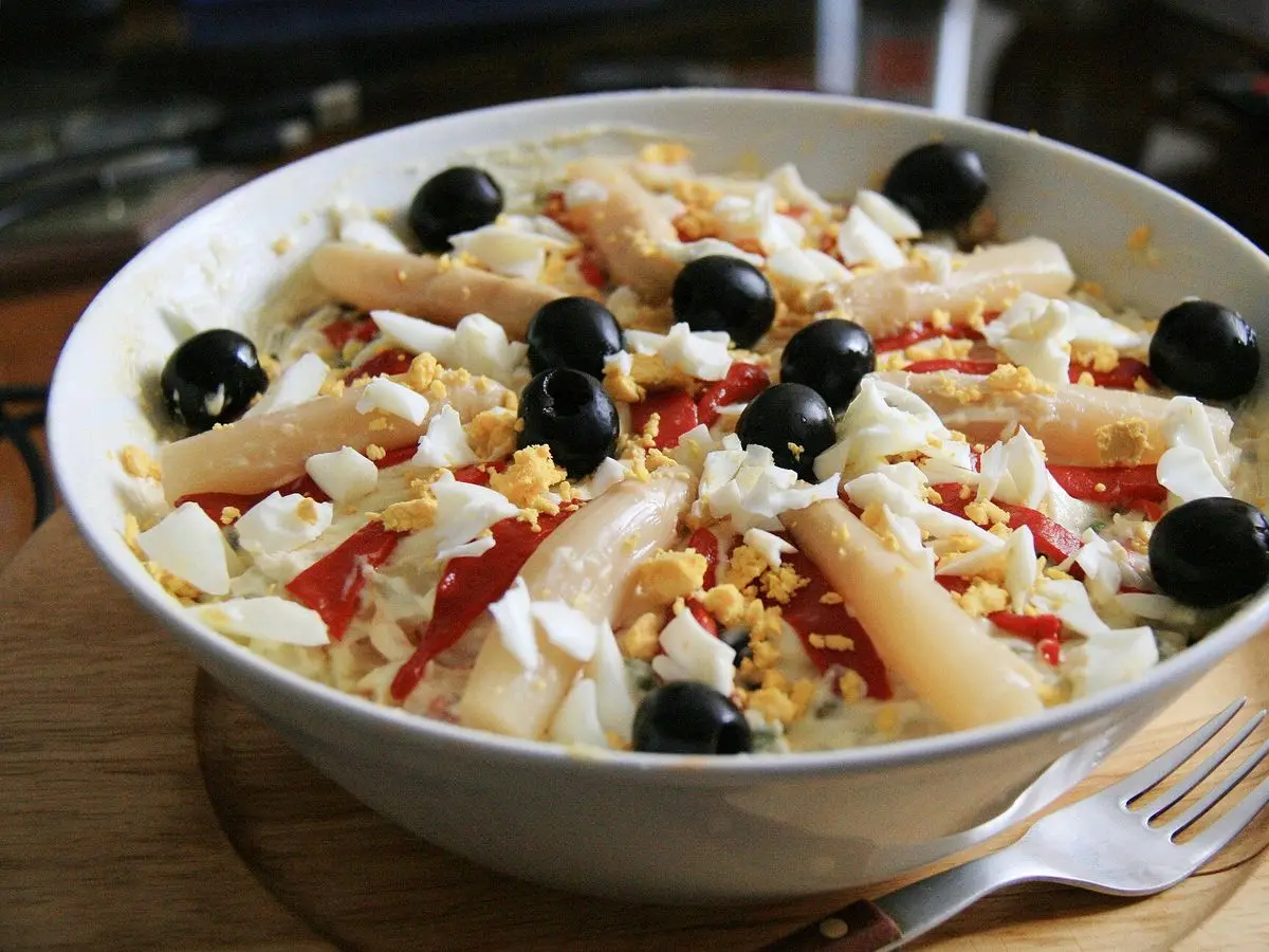 Cuenco de ensaladilla rusa con huevo duro, espárragos, pimiento y aceitunas negras