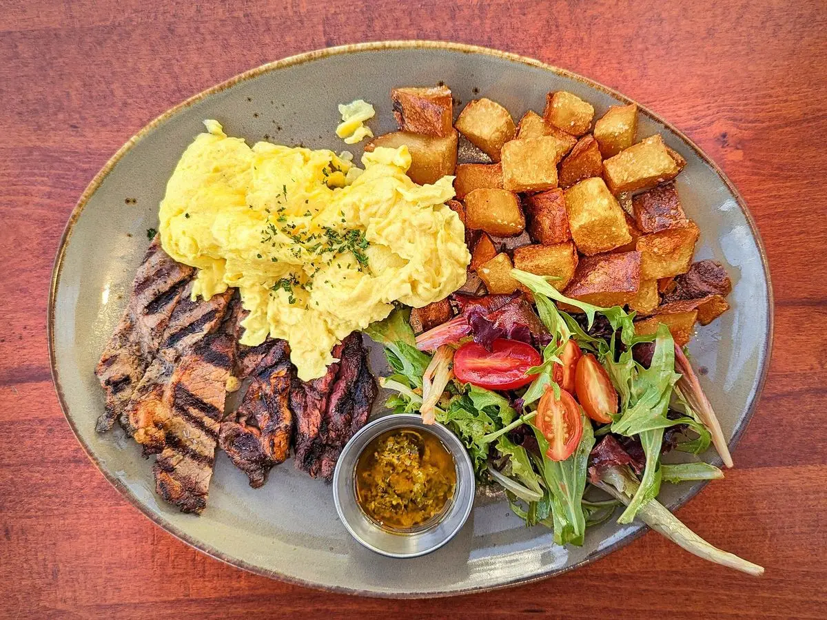 Plato con entraña a la parrilla, patatas doradas en dados, huevos revueltos, ensalada y salsa verde