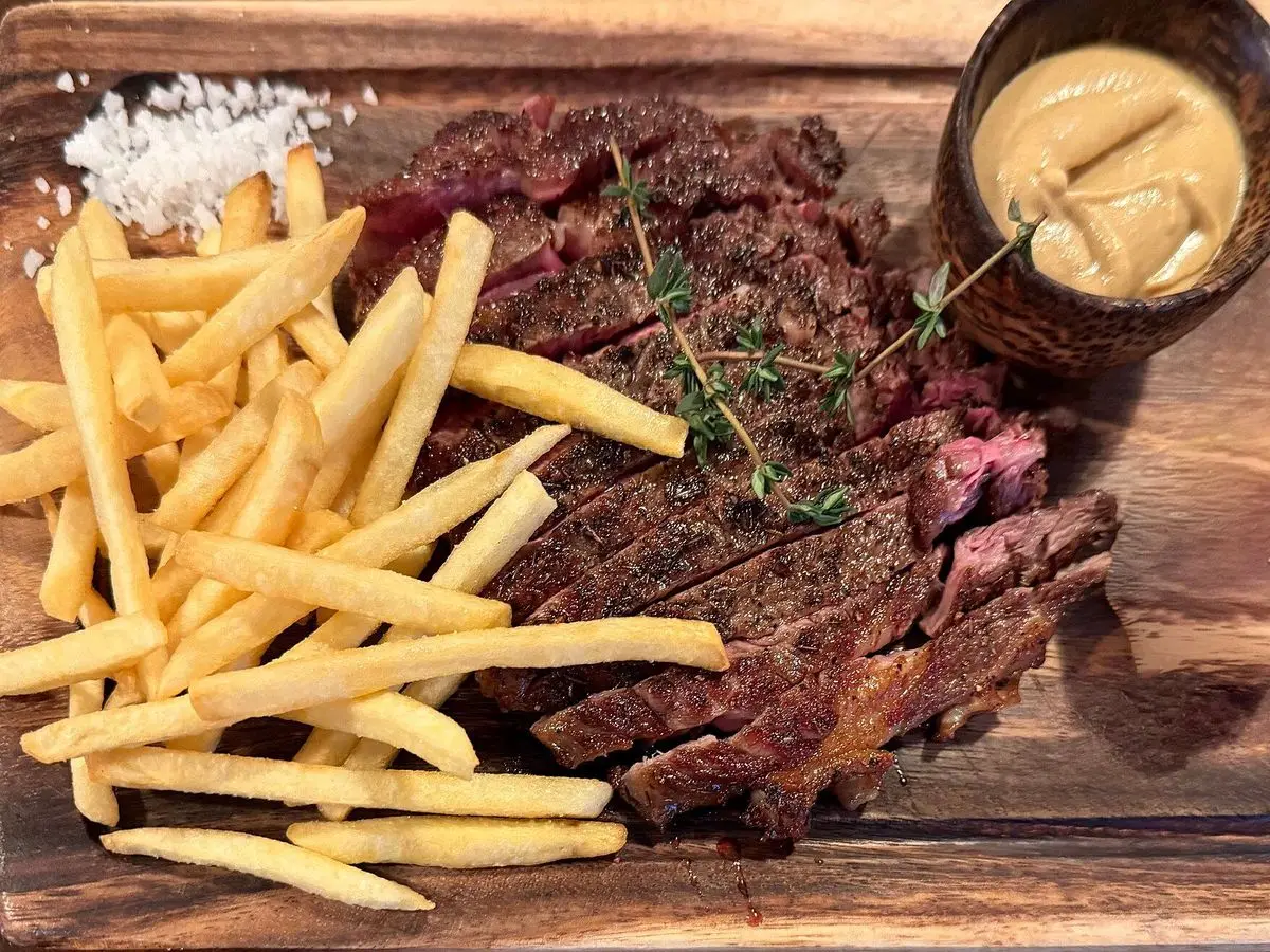 Entraña a la plancha cortada en tiras con patatas fritas y salsa en una tabla de madera