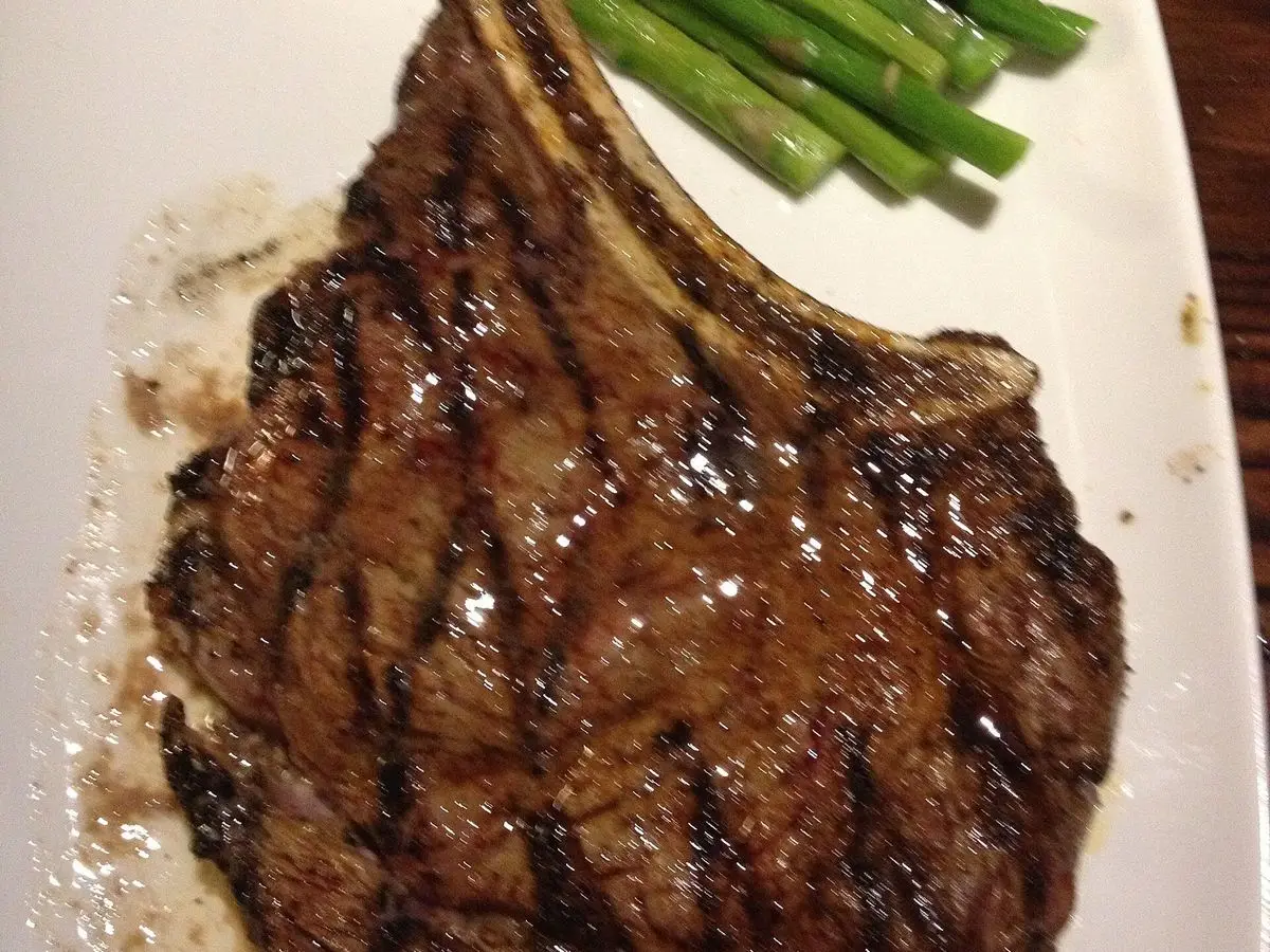 Entrecot de ternera a la plancha con marcas de parrilla y espárragos verdes en un plato blanco