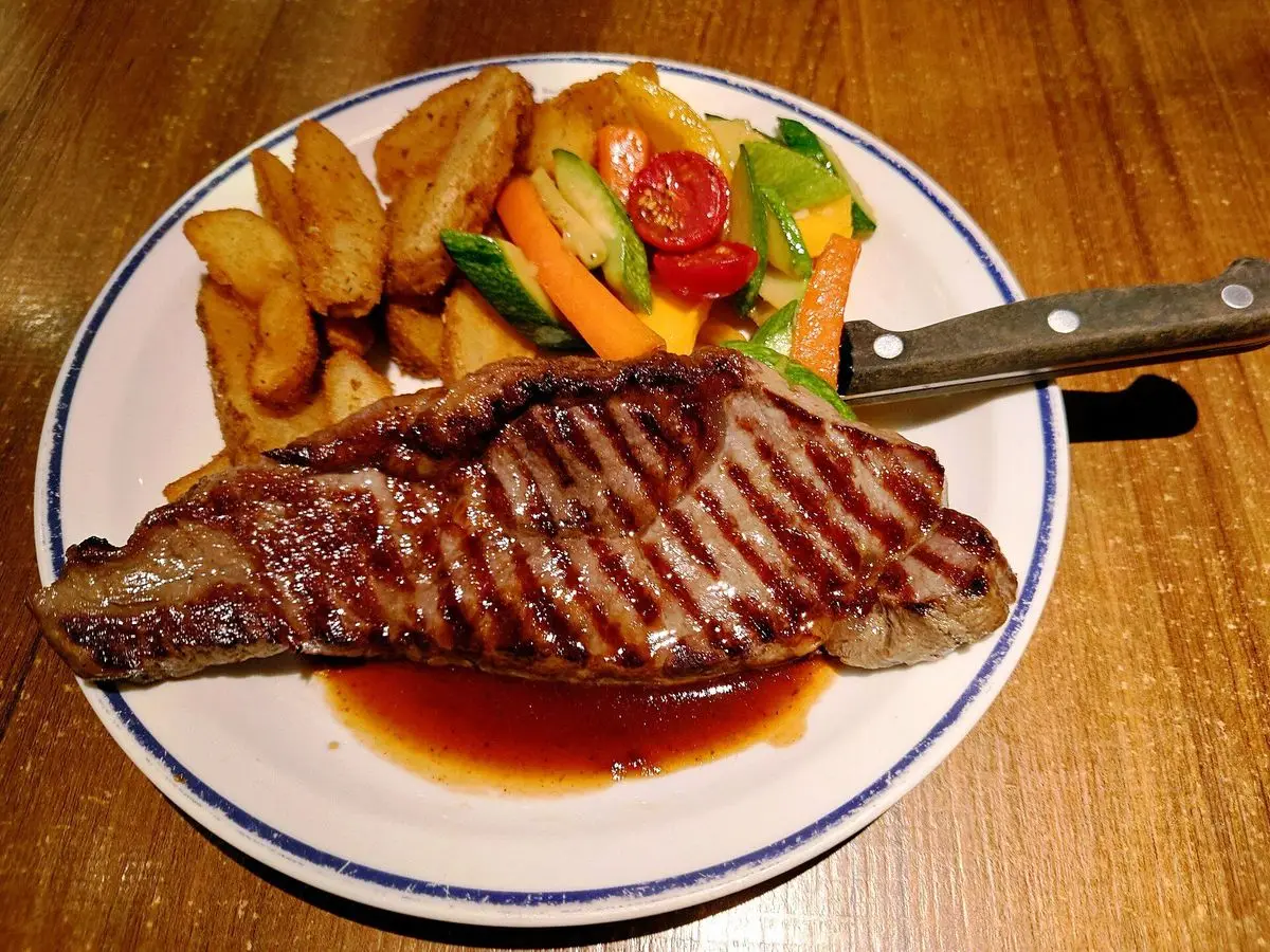 Entrecot a la plancha con salsa, patatas en gajos, pimiento, tomate y verduras en un plato