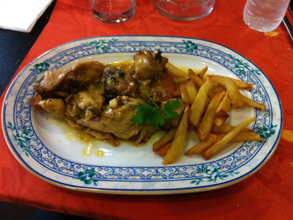Fuente ovalada con pollo guisado en salsa de almendra, patatas fritas y una rama de perejil