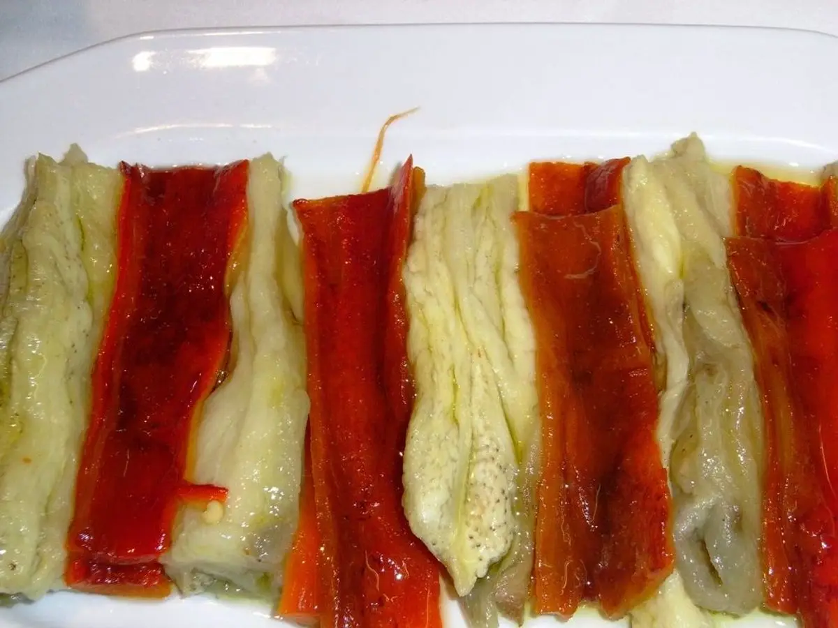 Tiras de berenjena y pimiento rojo asados dispuestas en fila sobre un plato blanco, escalivada