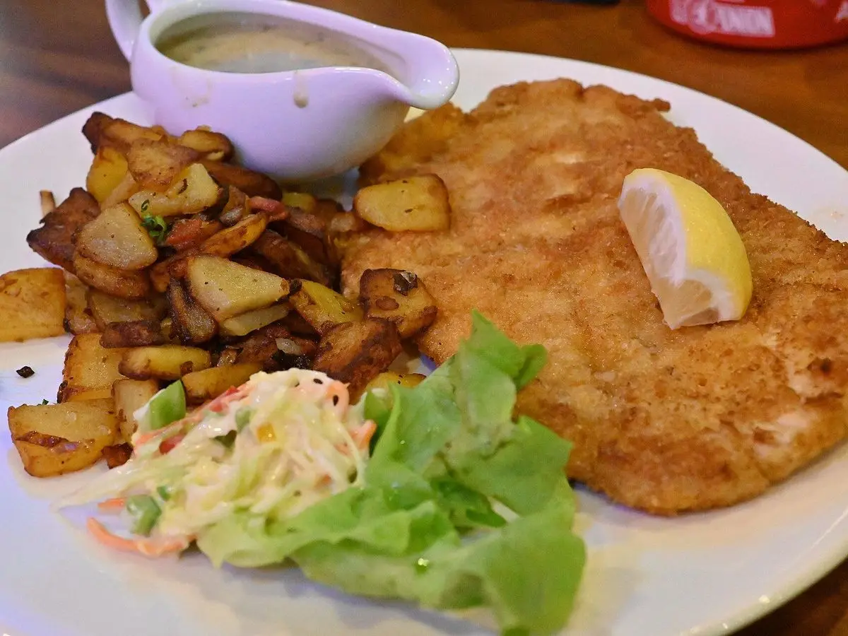 Escalope empanado con patatas asadas, ensalada de col, lechuga, gajo de limón y salsa