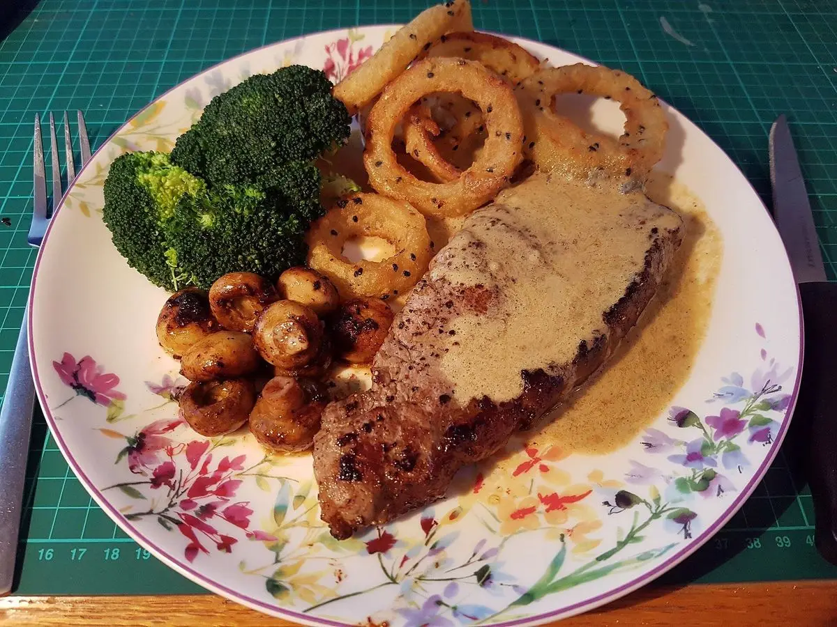 Filete de ternera con salsa cremosa, brócoli y champiñones sobre un plato floreado