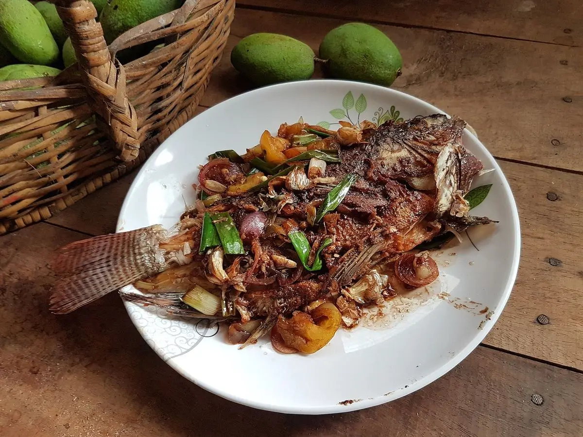 Pescado entero frito cubierto de escabeche de cebolla, pimiento y zanahoria en un plato blanco