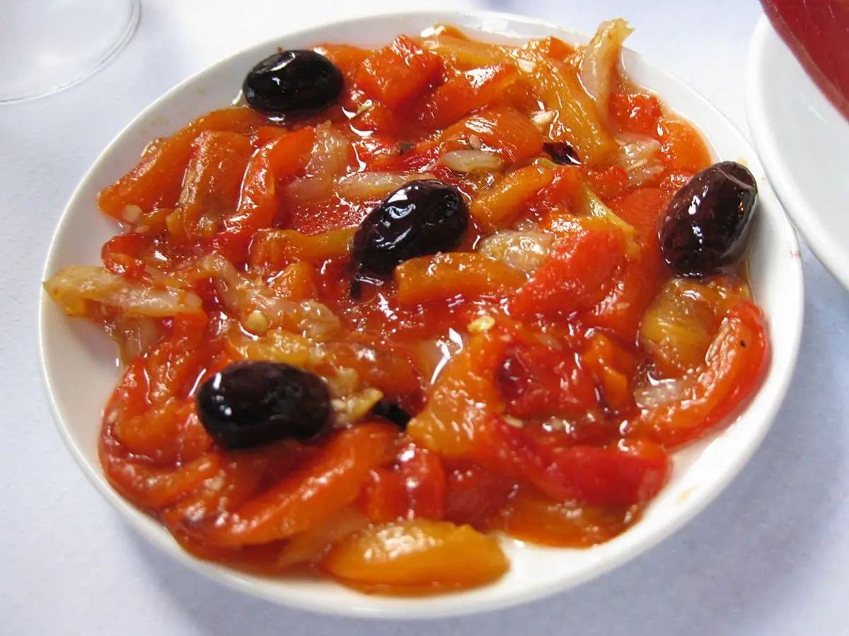 Plato blanco con tiras de pimiento rojo asado y aceitunas negras, aliñadas con aceite