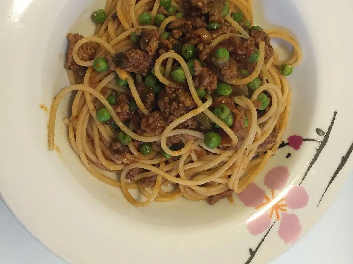 Espaguetis con salsa de carne picada y guisantes en un plato blanco