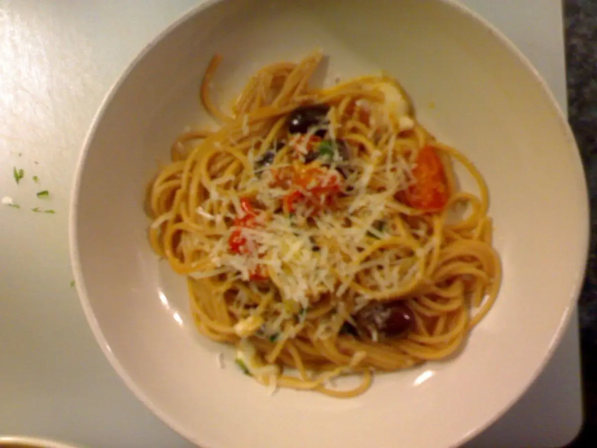 Cuenco blanco de espaguetis con tomate, aceitunas y polvo de pan o queso rallado por encima