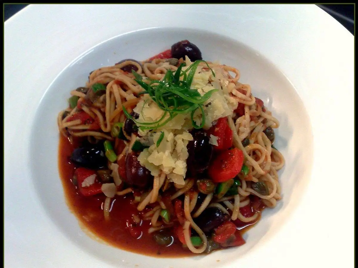 Plato hondo de espaguetis con salsa de tomate, aceitunas negras y perejil