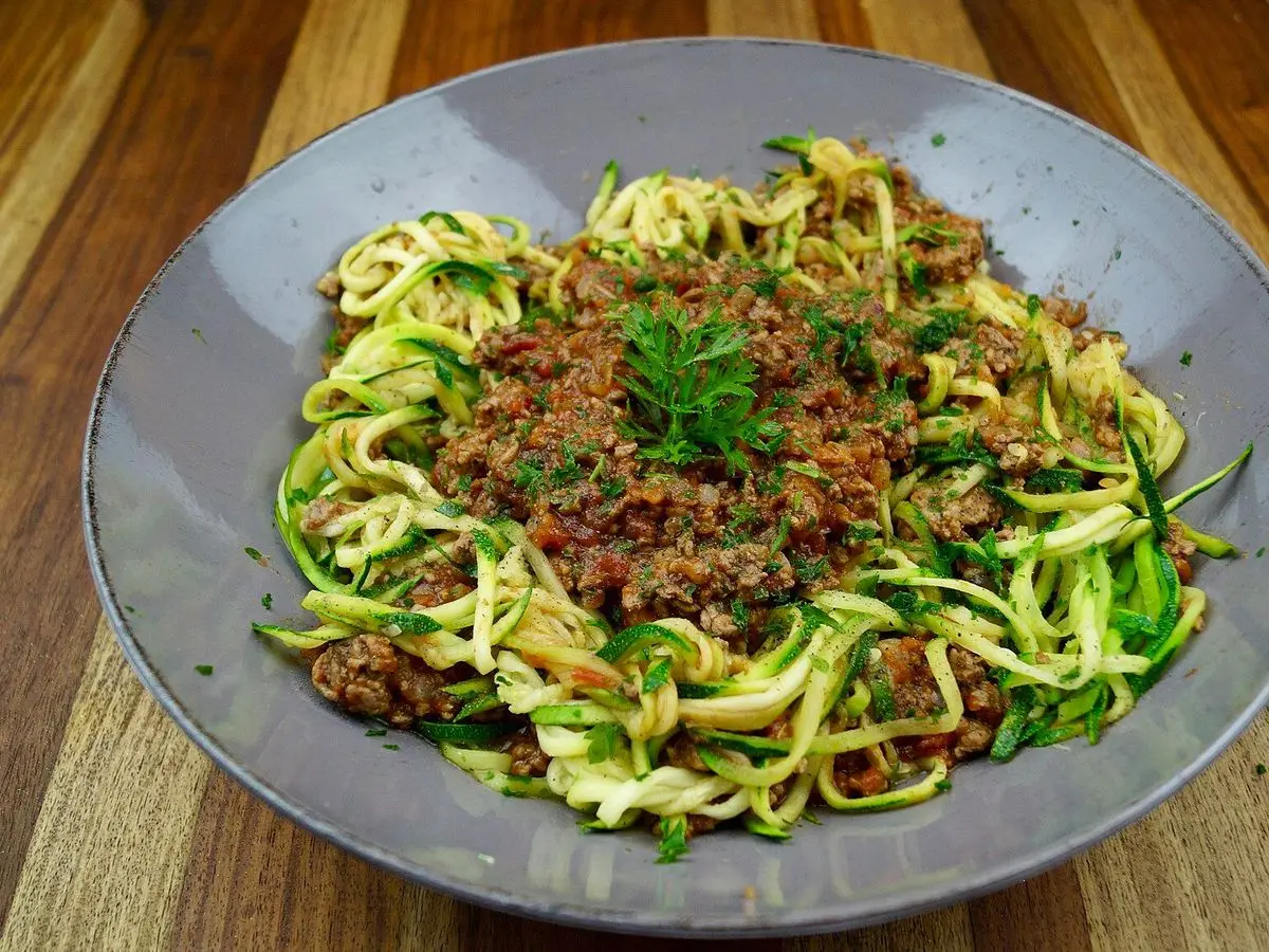 Cuenco gris de espaguetis de calabacín con salsa boloñesa de carne y una hoja de perejil