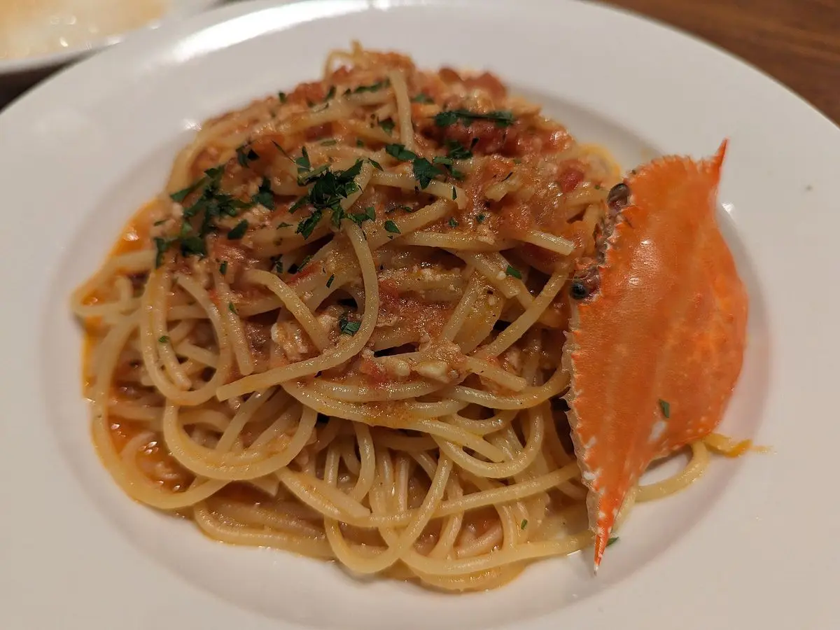 Plato de espaguetis con carne de cangrejo, perejil y una pinza de cangrejo en un plato blanco