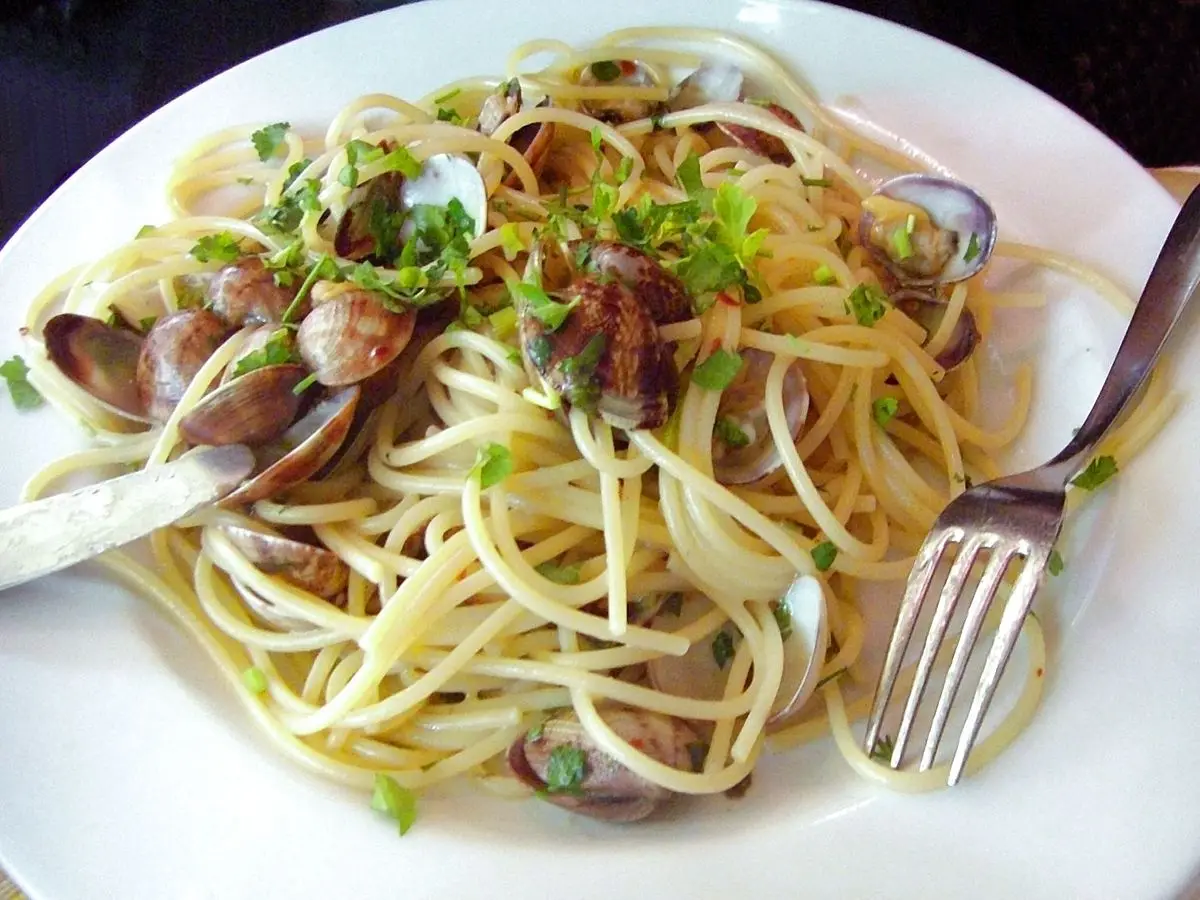 Plato de espaguetis con almejas, perejil y aceite, con un tenedor