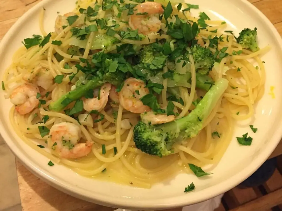 Espaguetis con langostinos, brócoli y abundante perejil picado en un plato blanco