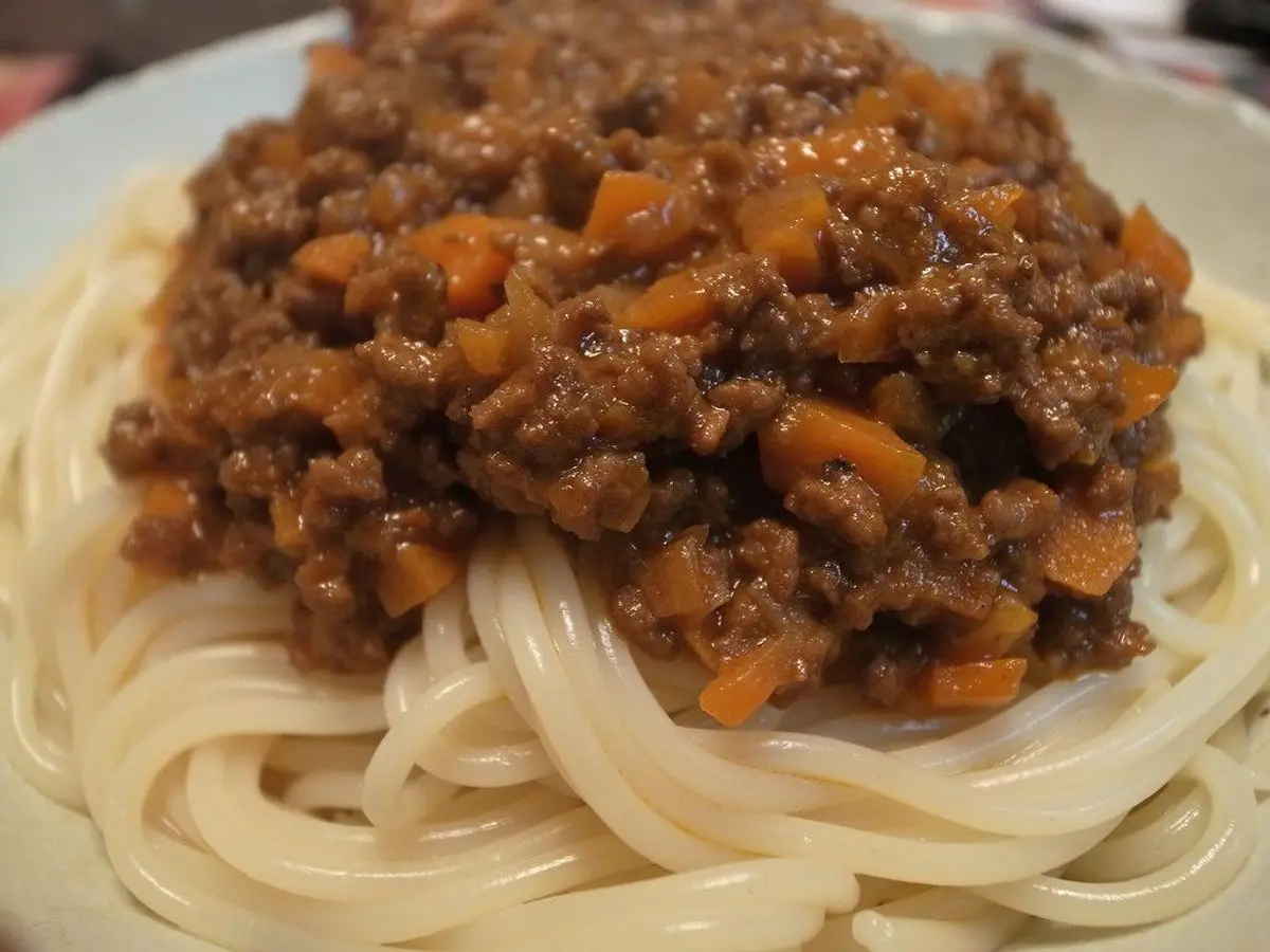 Espaguetis con una espesa salsa boloñesa de tomate con trocitos de zanahoria en un plato blanco