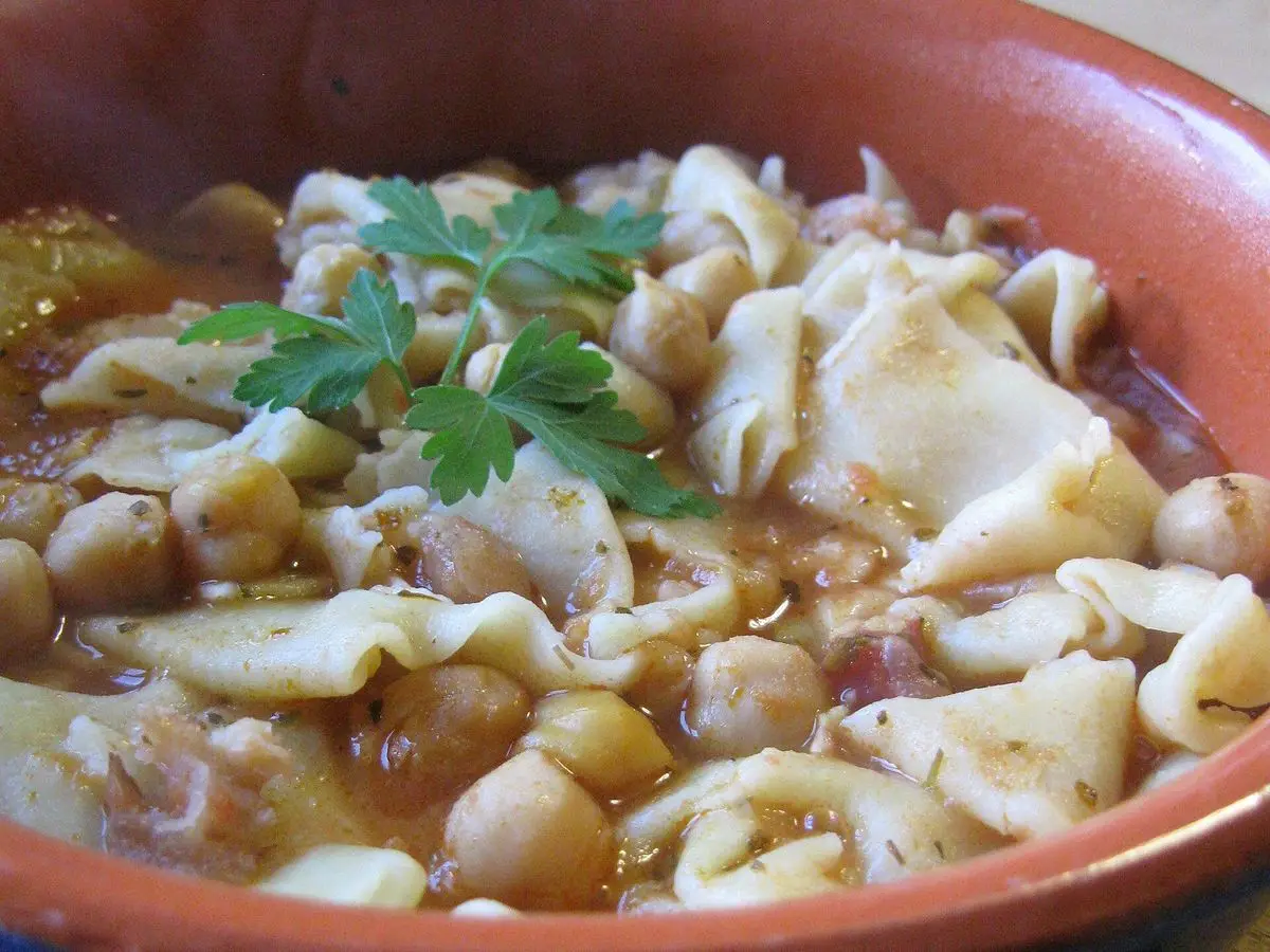 Cuenco de barro con pasta y garbanzos en caldo de tomate con perejil fresco por encima