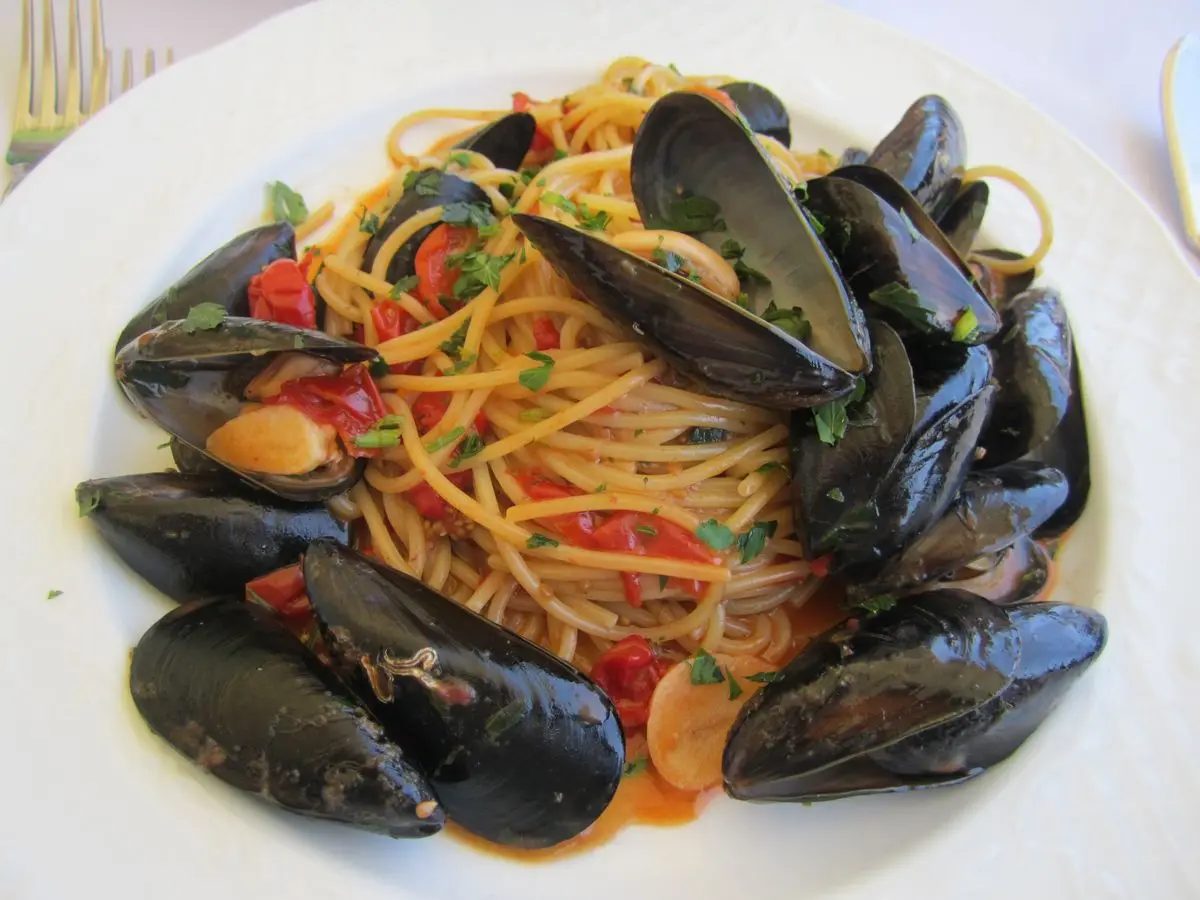 Espaguetis con mejillones en su concha, trocitos de tomate y perejil picado en un plato blanco