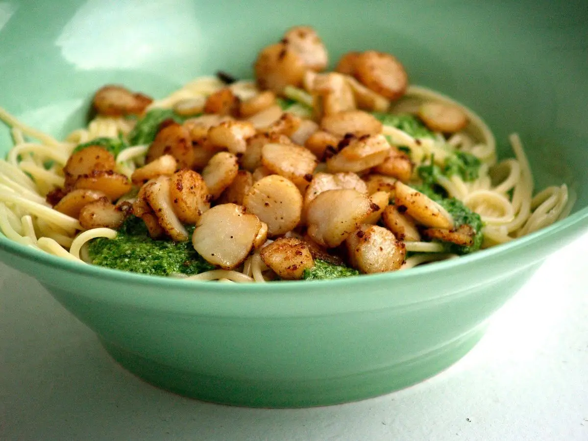 Cuenco verde de espaguetis con pesto y vieiras doradas por encima