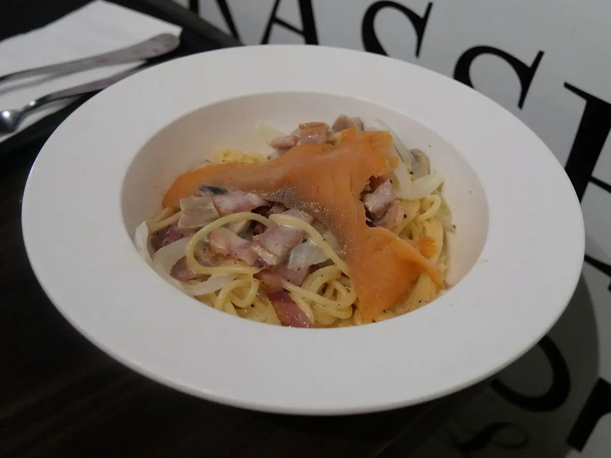Plato hondo blanco de espaguetis con láminas de salmón ahumado y salsa cremosa