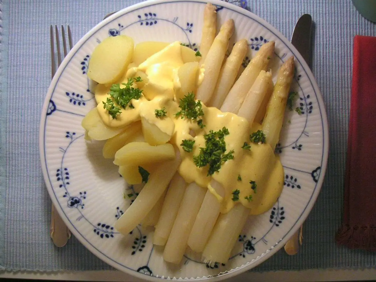 Espárragos blancos con salsa holandesa, patatas cocidas y perejil en un plato blanco con dibujos azules