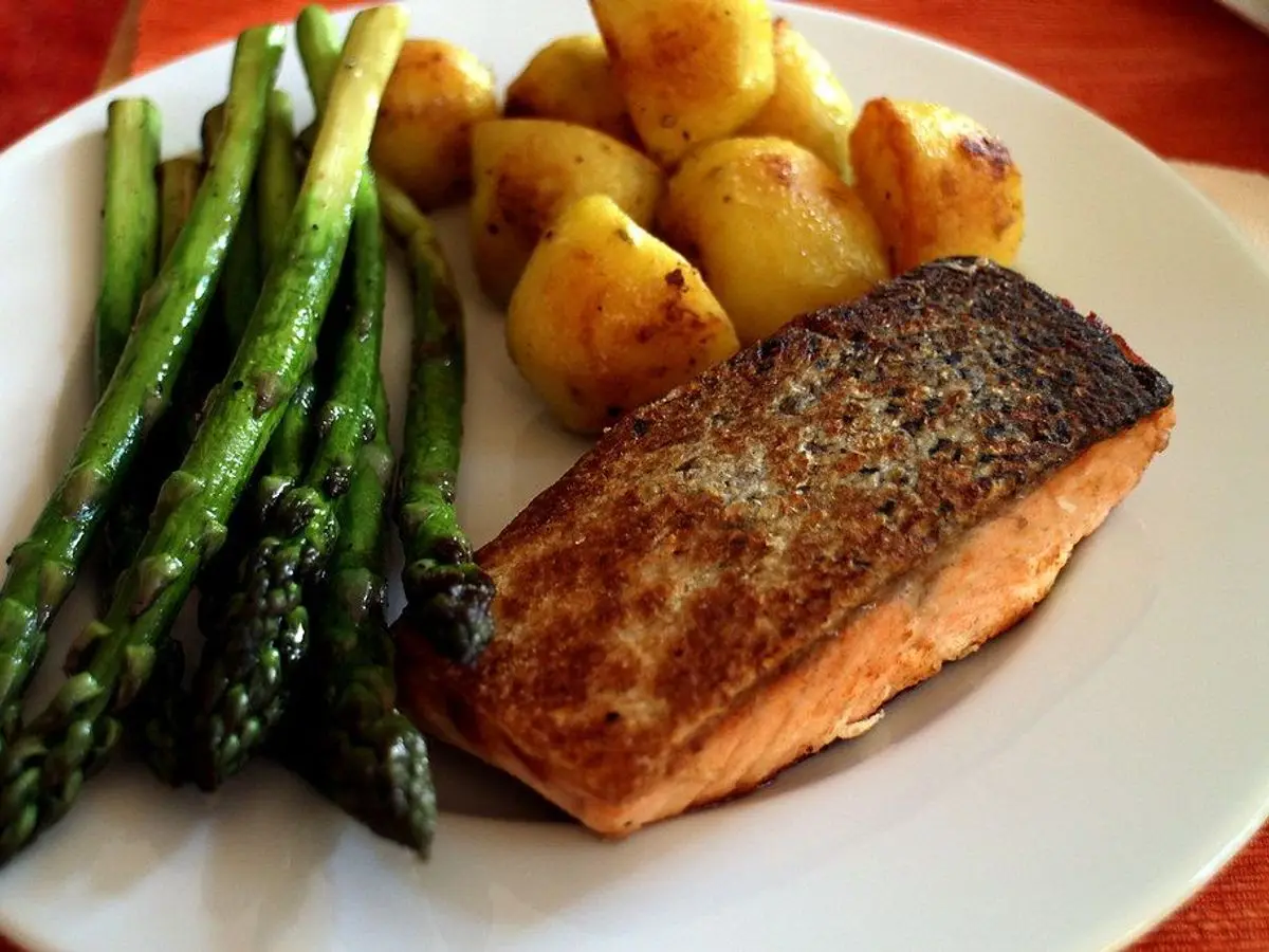Filete de pescado a la plancha con espárragos verdes y patatas pequeñas asadas en un plato blanco