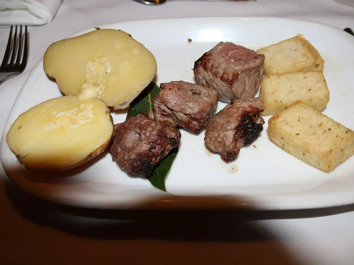 Dados de ternera asada con patatas hervidas y cubos de polenta frita sobre una hoja de laurel en un plato blanco