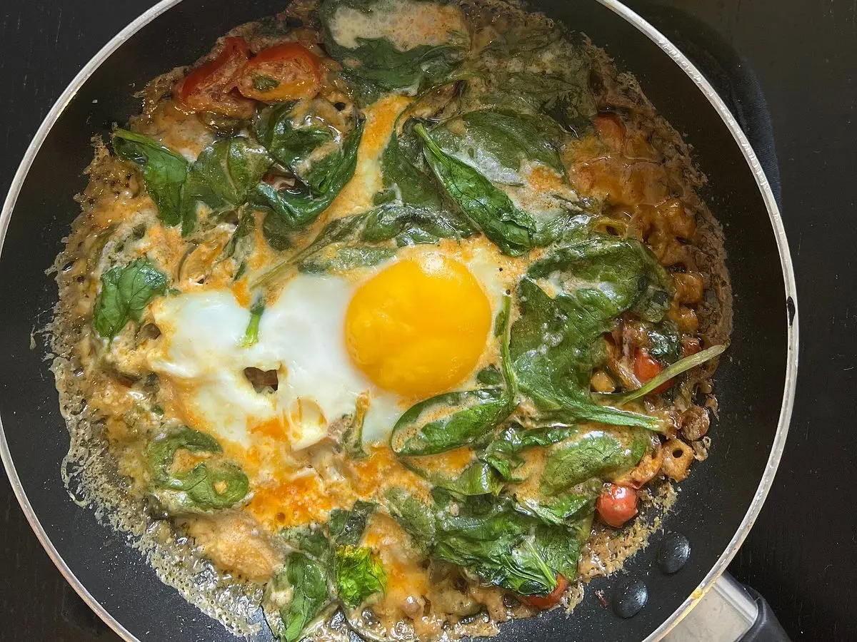 Sartén con espinacas salteadas, unos tomates cherry y un huevo cuajado en el centro