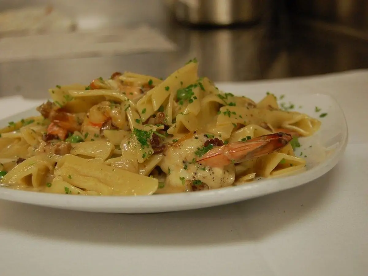 Plato blanco de pasta larga con gambas y hierbas picadas