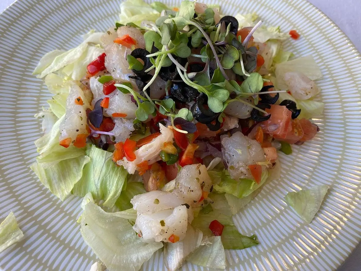 Esqueixada catalana de bacalao desmigado con tomate, cebolla, aceitunas negras y brotes sobre lechuga en un plato