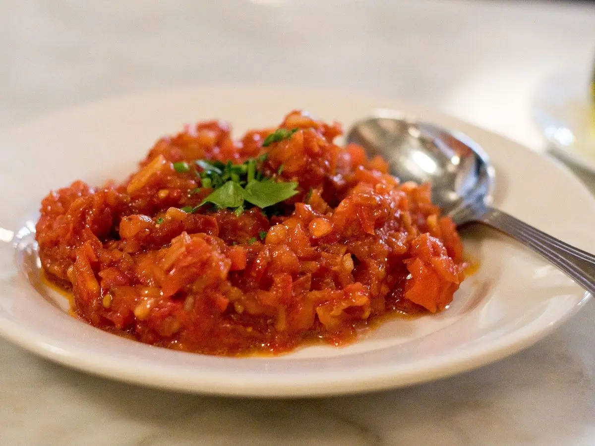 Plato blanco con ezme turca, picadillo picante de tomate y cebolla con perejil, y una cuchara