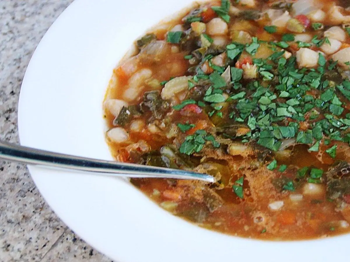 Plato hondo de guiso de alubias blancas con col rizada, zanahoria y tomate, con perejil picado por encima