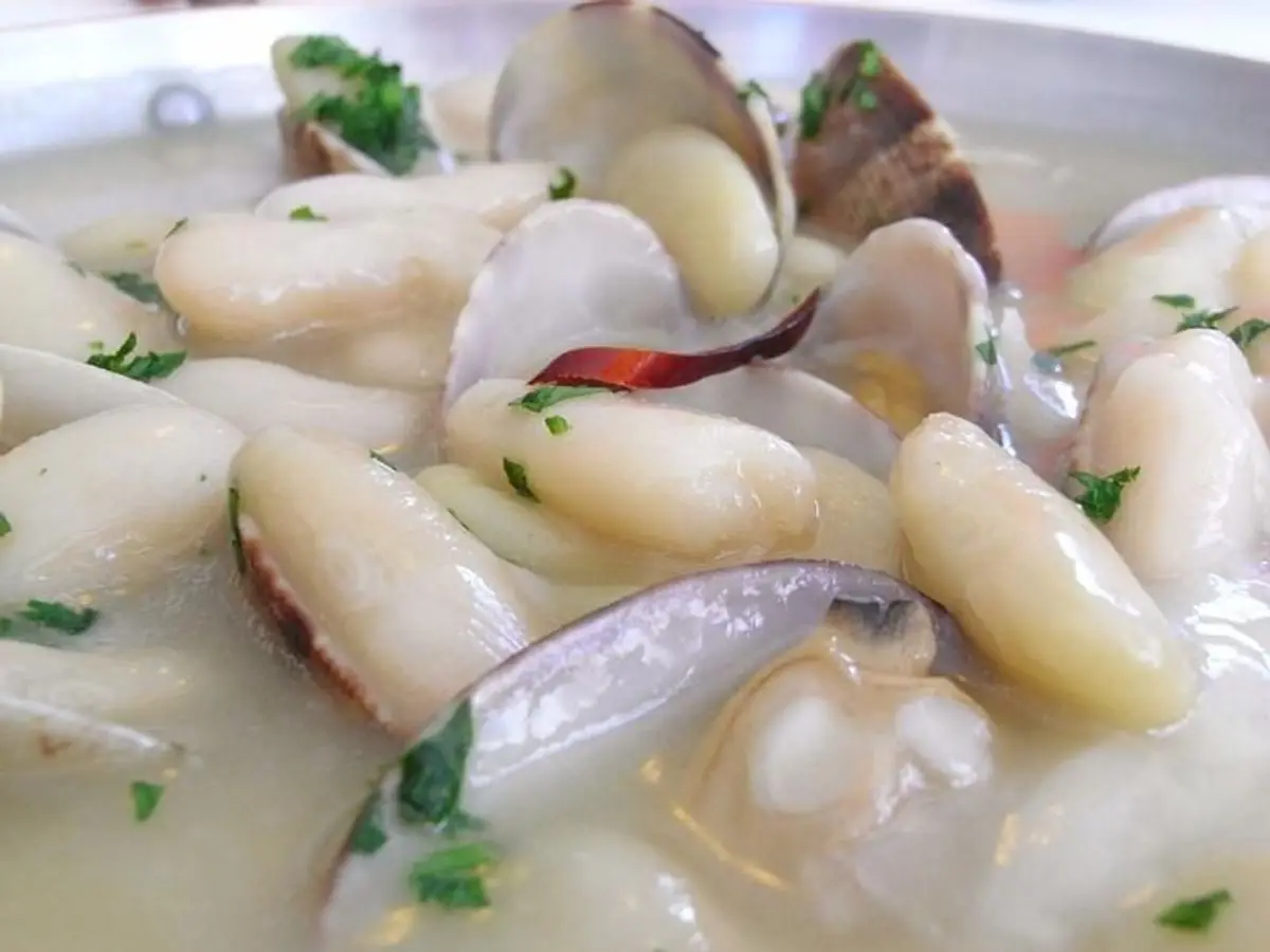 Fabes blancas guisadas con almejas abiertas, un trozo de guindilla y perejil picado en caldo claro