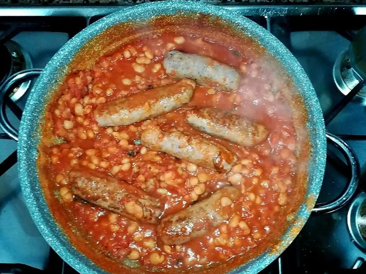 Sartén azul con alubias blancas en salsa de tomate y salchichas