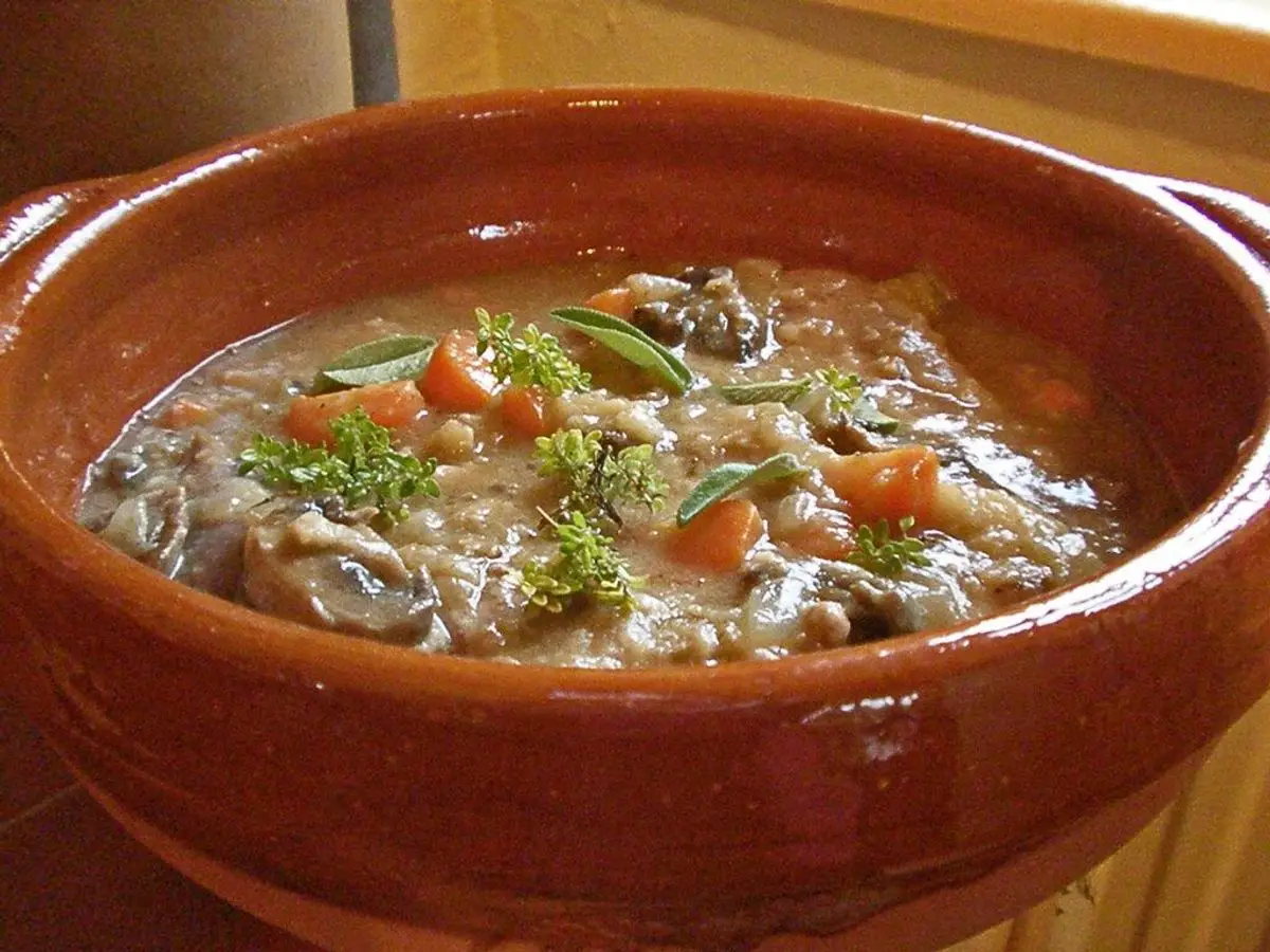 Cazuela de barro con estofado de faisán, zanahoria en dados, champiñones y ramitas de tomillo y salvia