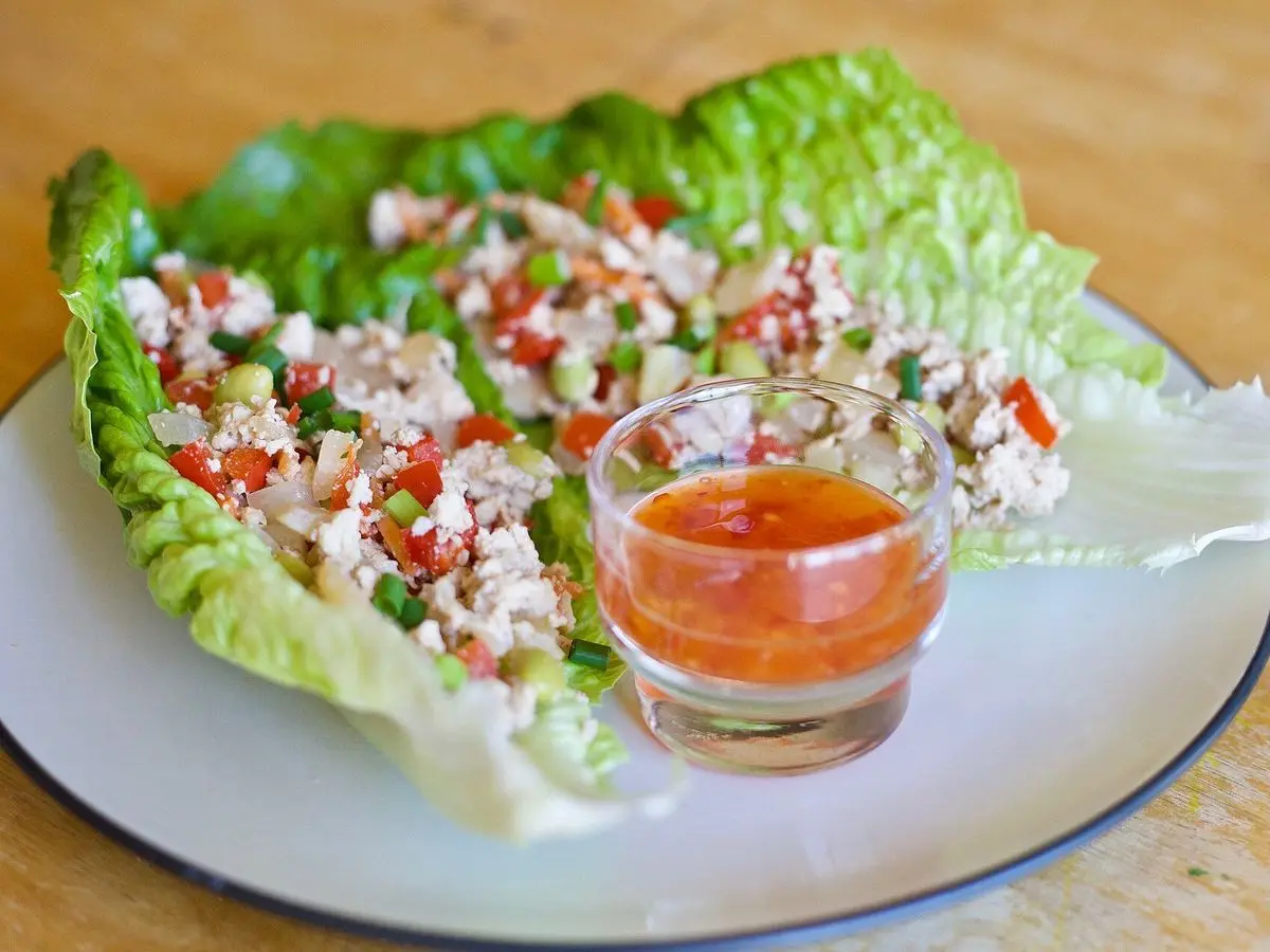 Hojas de lechuga rellenas de pollo picado con tomate y salsa picante en un plato blanco