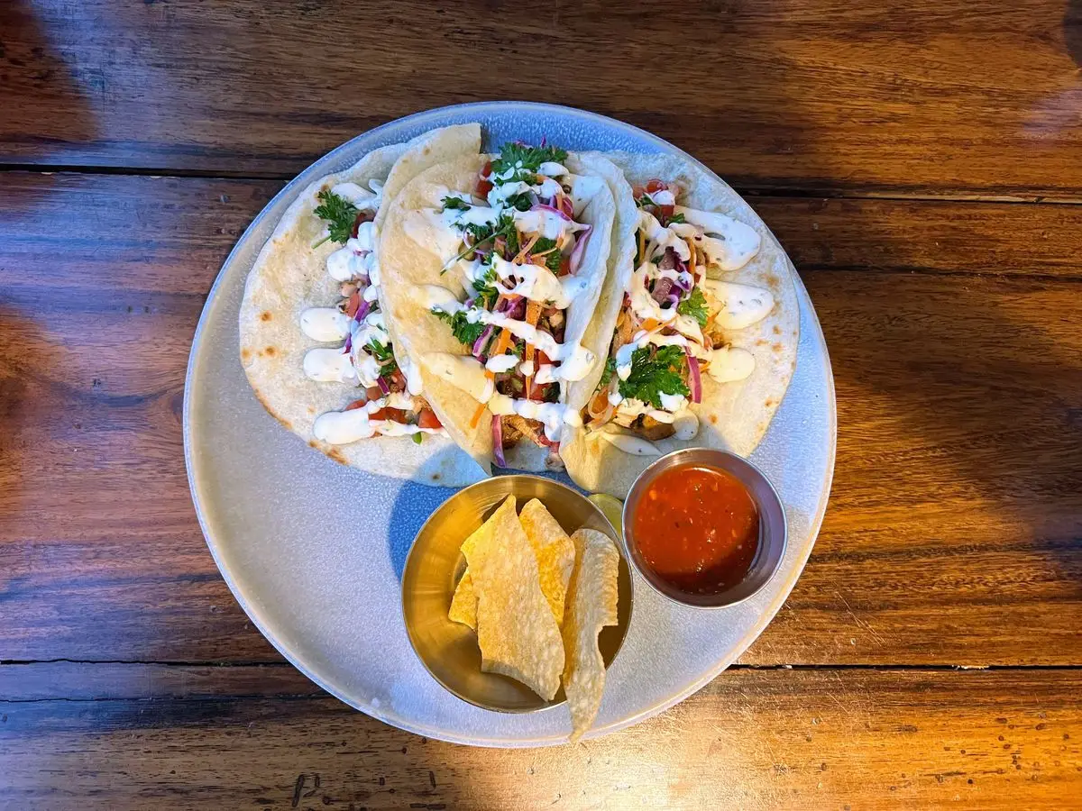 Tres tortillas de trigo rellenas de carne, col y cilantro con salsa blanca, junto a totopos y salsa roja