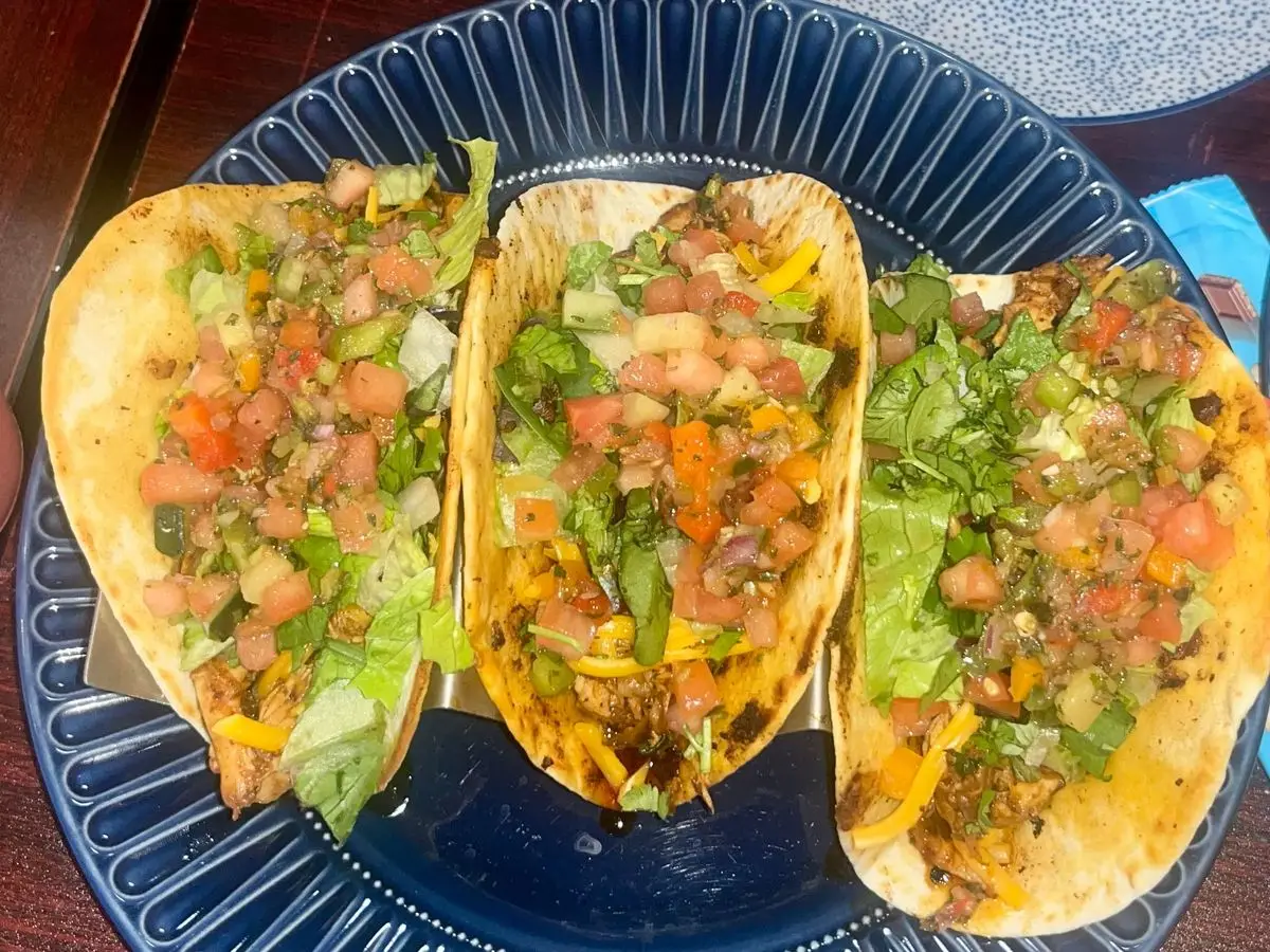Tres tortillas de trigo rellenas de tomate picado, lechuga, pimiento y hierbas en un plato azul