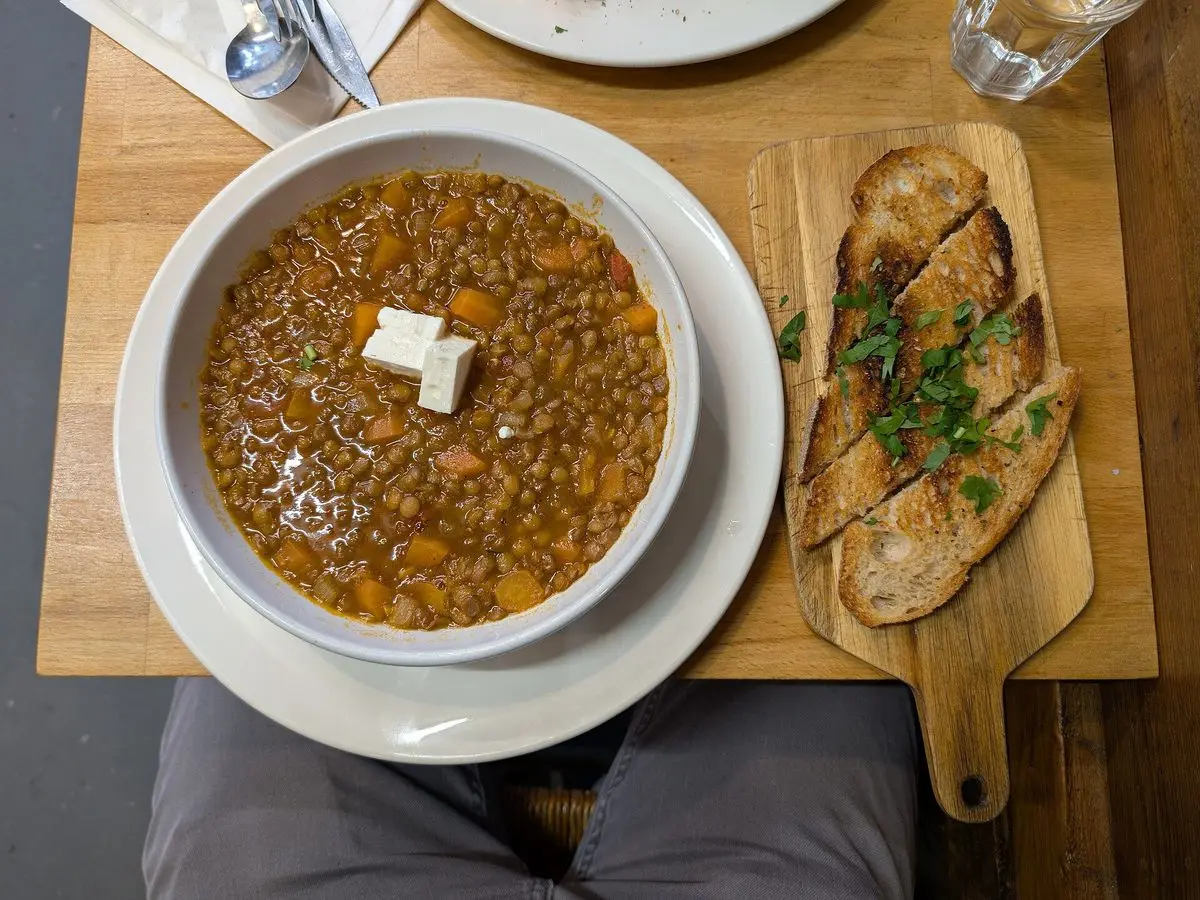 Plato hondo de sopa de lentejas con tomate y dos dados de feta, junto a pan tostado con hierbas
