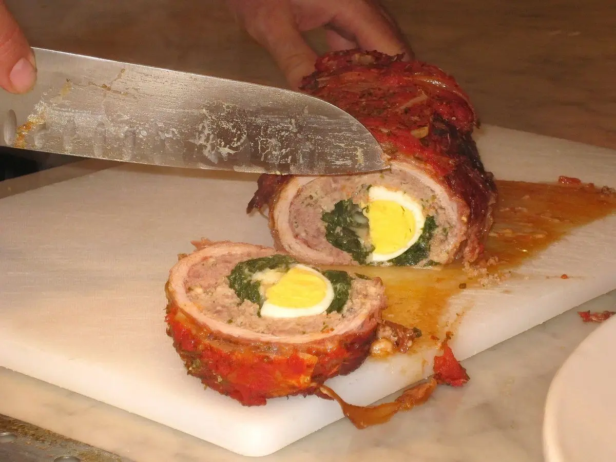Rollo de carne asado relleno de espinacas y huevo duro, cortado en rodajas sobre una tabla blanca