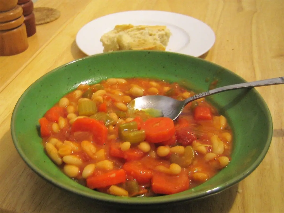 Cuenco verde de sopa de alubias blancas con tomate, zanahoria y apio y una cuchara