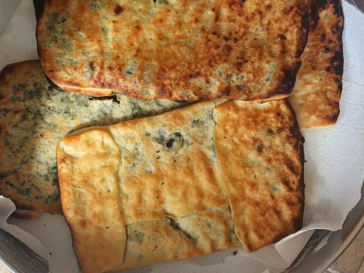 Fatayer horneados, empanadas de masa dorada rellenas de espinacas, servidos sobre papel