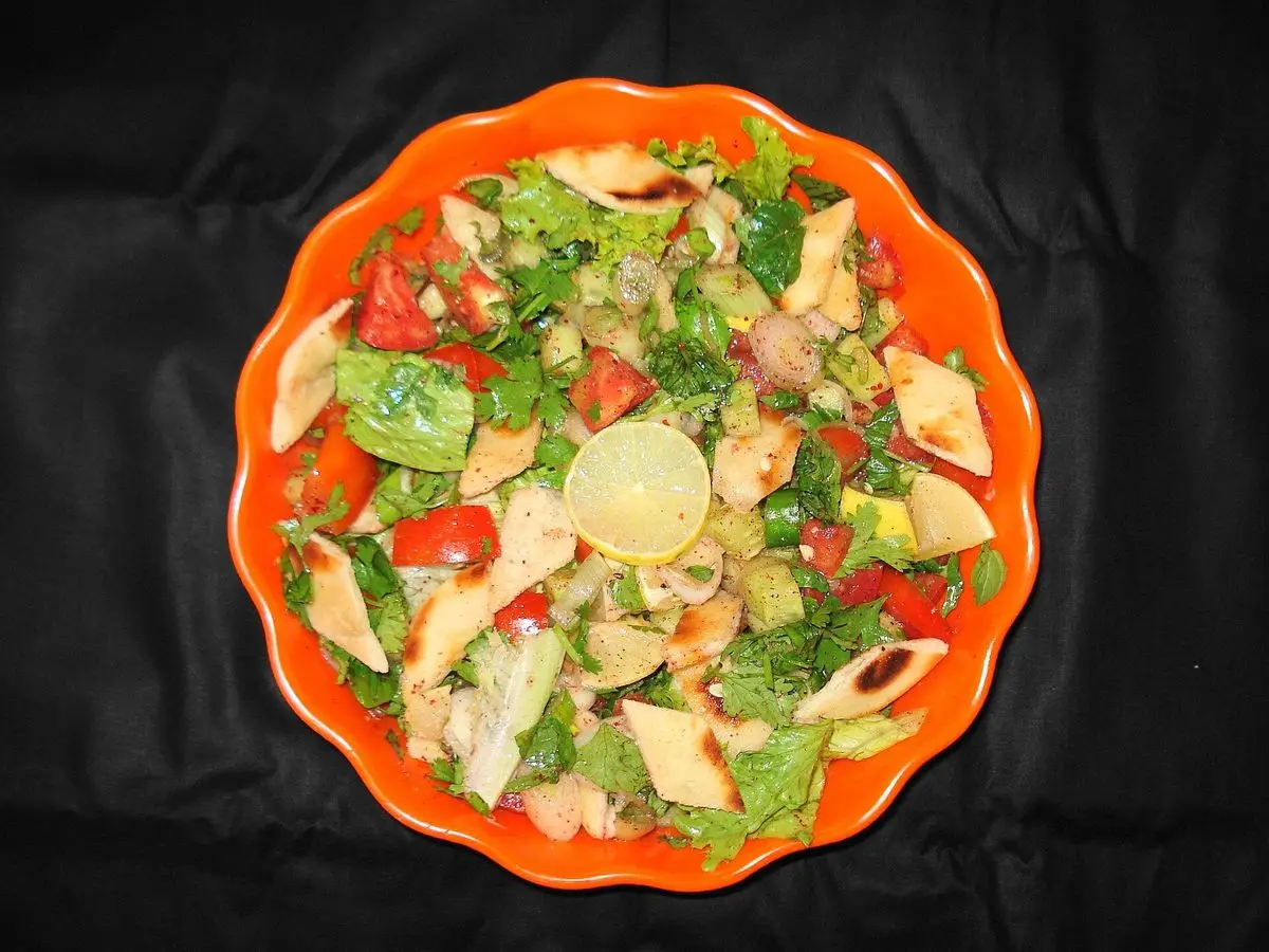 Ensalada fattoush con tomate, pepino, lechuga y trozos de pan tostado en un plato naranja