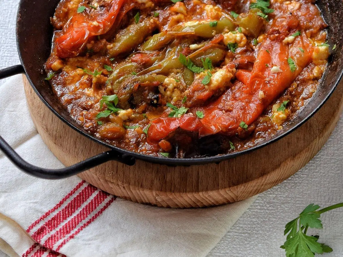 Cazuela negra con pimientos asados y tomate en salsa roja con requesón y hierbas por encima
